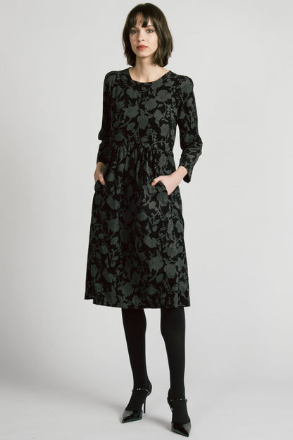 A woman wearing the Virgo Dress by Allison Wonderland in Floral, a babydoll style dress in floral printed fine wale corduroy with bracelet length sleeves and a midi length. She's standing against a white background. 