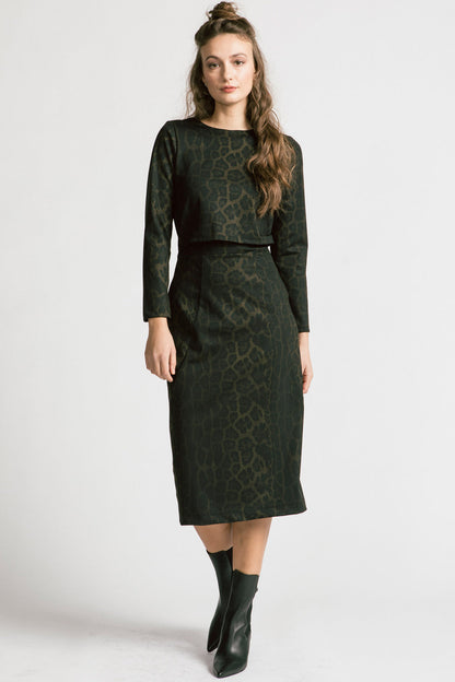  A woman wearing the Allison Wonderland Expectations dress in Leopard, featuring an opening at the front and attached back, a two-way back zipper, V-neckline at the back, long sleeves, and midi-length. She is standing in front of a white background. 