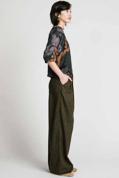 Side view of a woman wearing the Flash Blouse by Allison Wonderland in Horse Print, featuring 3/4 dropped raglan sleeves, a boat neck with gathers at the shoulders, and a loose fit. She is wearing it with the Memory Pant in Herringbone and standing in front of a white background. 