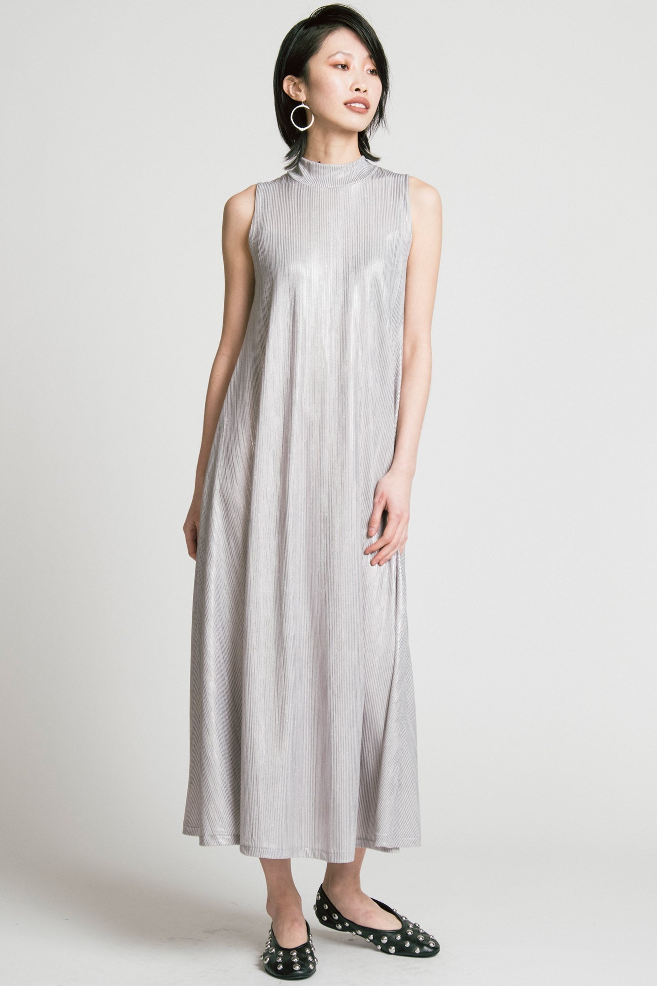 A woman wearing the Swing Dress by Allison Wonderland in Silver, a sleeveless mock neck maxi dress in shimmery fabric. 