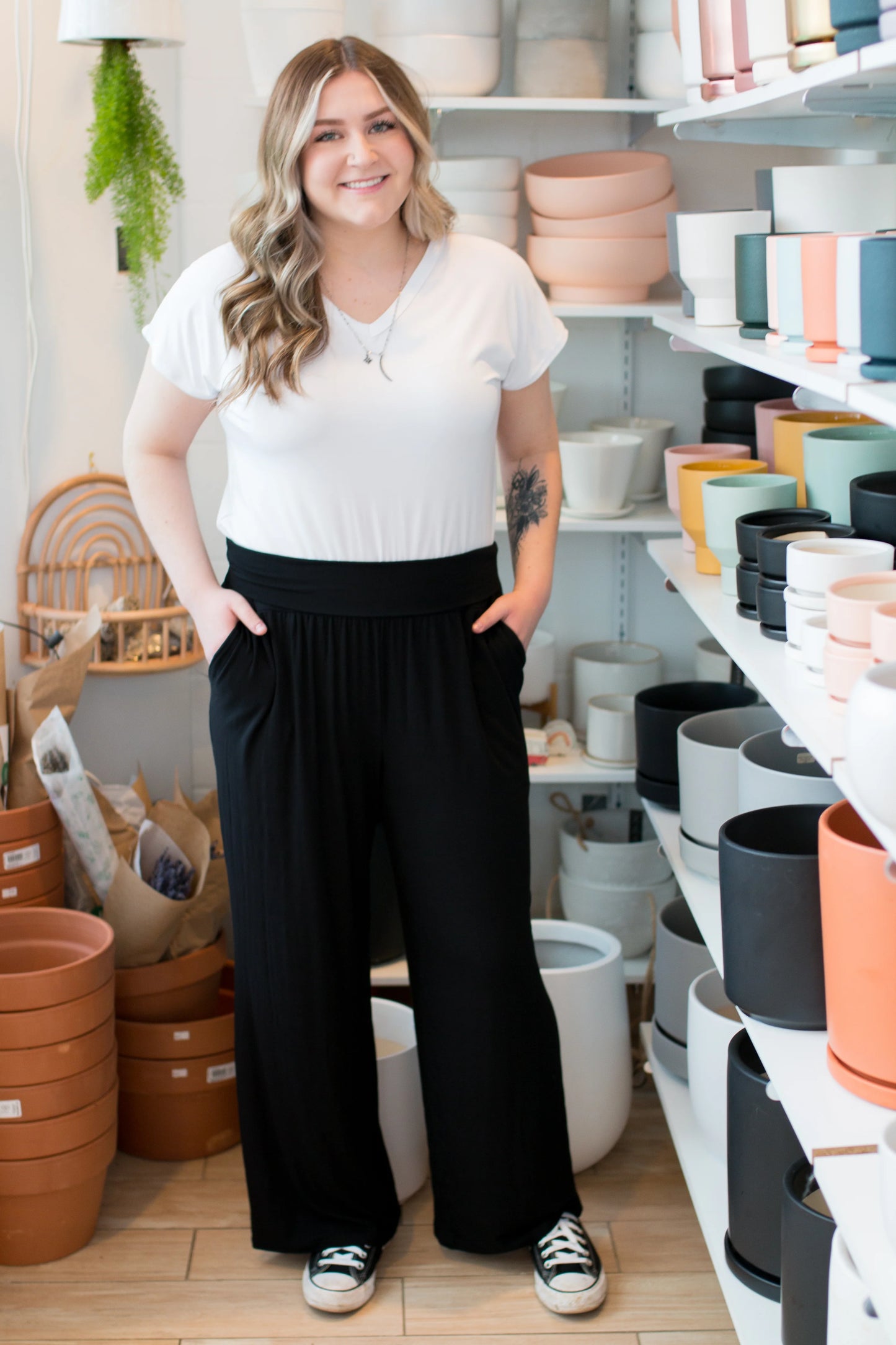 A woman wearing the Bree Wide Leg Pants by Ang Hill in Black, cropped wide-legged pants with a high elastic waist band and deep pockets. She is wearing them with a white t-shirt and standing in a pottery studio. 
