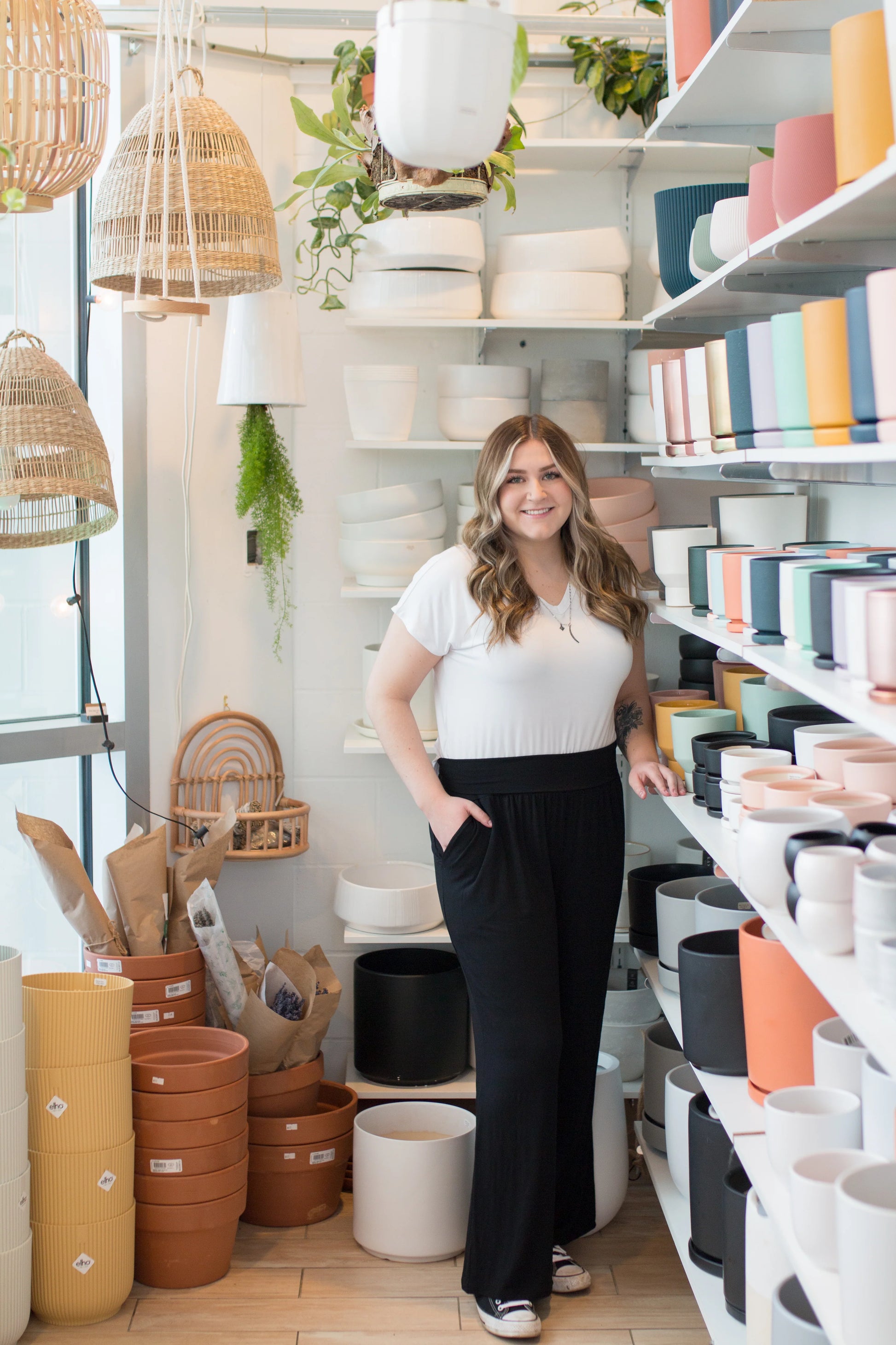 A woman wearing the Bree Wide Leg Pants by Ang Hill in Black, cropped wide-legged pants with a high elastic waist band and deep pockets. She is wearing them with a white t-shirt and standing in a pottery studio. 