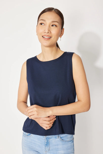 A woman wearing the Baie Cami by Canopée in Navy, a bamboo French Terry tank with a high neck and loose fit. She is wearing it with jeans and standing in front of a white background. 