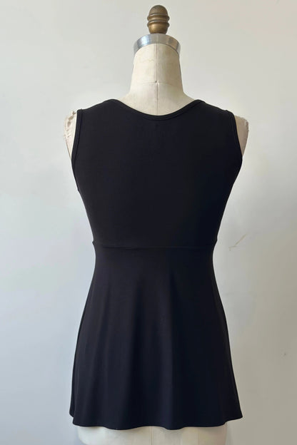 A back view of the Nira Top by Kollontai in Black, a sleeveless top with a wide neck, an empire waist, and a cut that's fitted through the bodice and flares away from the torso, is shown on a mannequin against a white background. 