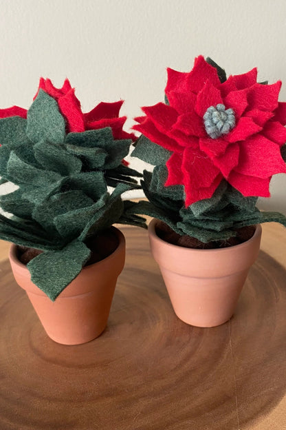 The Holiday Felt Poinsettia by ForgetBKnot is shown on a log against a white background. 