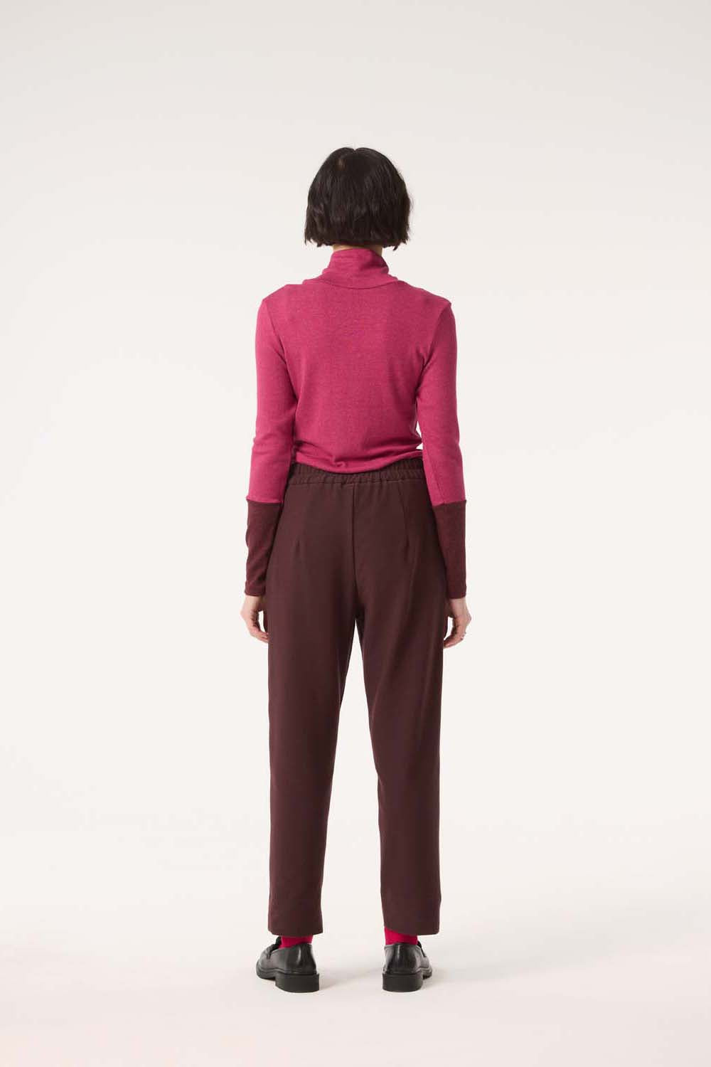 Back view of a woman wearing the Belief Pants by Cokluch in Shiraz with a pink top, standing in front of a white background . 