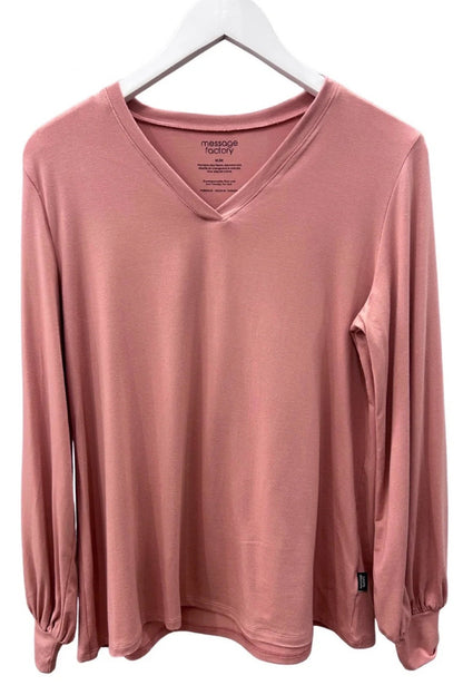 The Belmina Long Sleeve Top by Message Factory in Pink, with a small v-neck, long sleeves with puffed cuffs, and a relaxed fit, is shown hanging in front of a white background. 