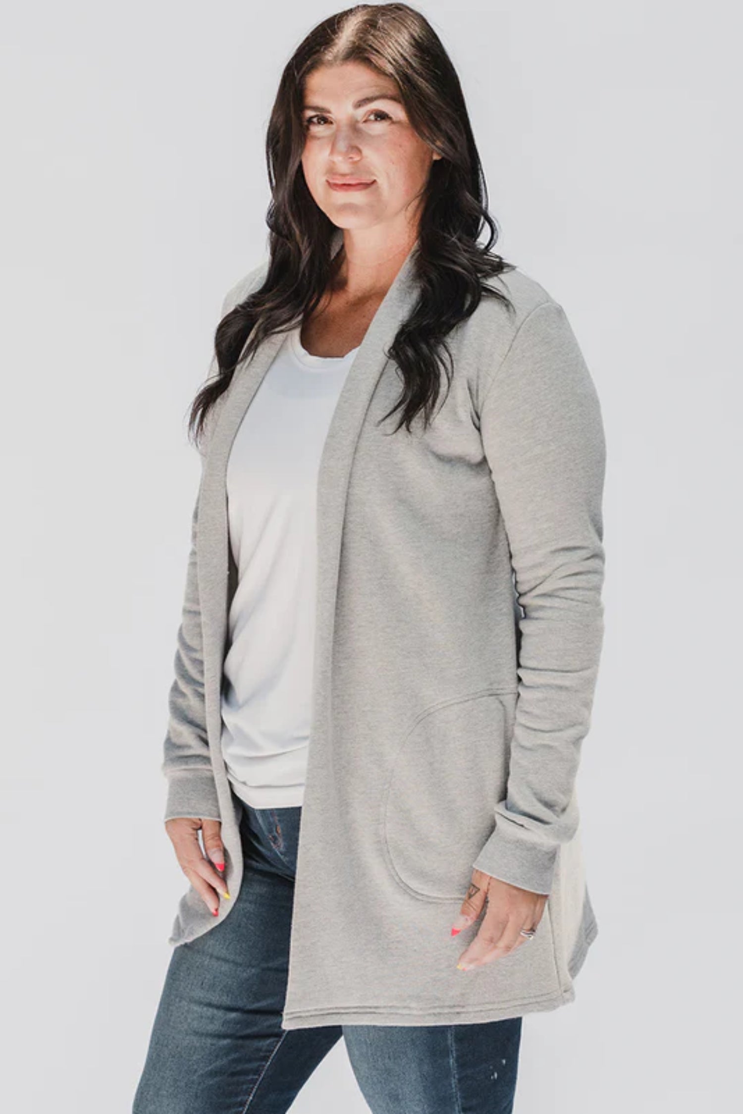 A woman wearing the Classic Briton Cardigan by Blondie Apparel in Grey with jeans and a white t-shirt, standing in front of a white background 