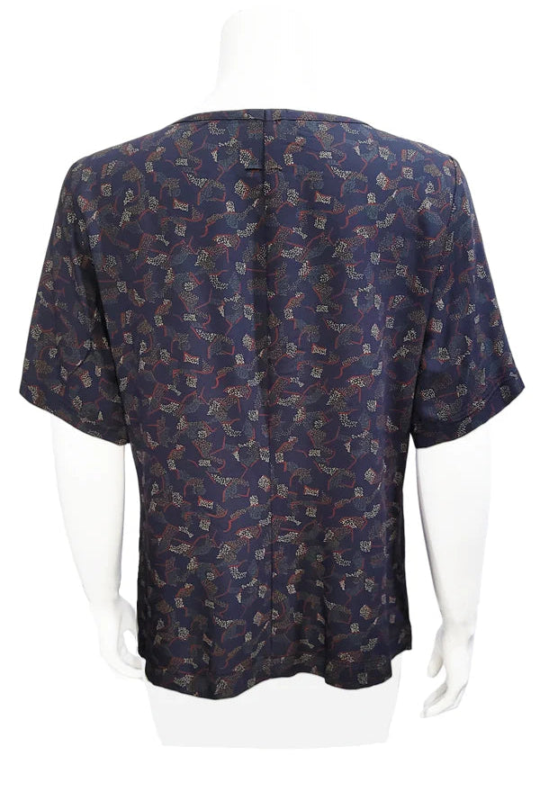 A back view of the Cecil Box Blouse by Mandala in Night Hex print is shown on a mannequin against a white background. It has a high neckline, wide 1/2 sleeves, and a side hem slit detail.