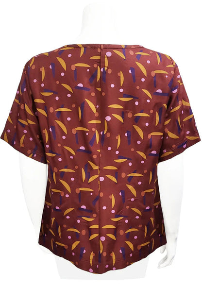 A back view of the Cecil Box Blouse by Mandala in Playtime Rust print is shown on a mannequin against a white background. It has a high neckline, wide 1/2 sleeves, and a side hem slit detail.