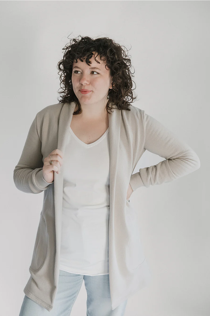 A woman wearing the Classic Briton Cardigan by Blondie Apparel in Stone with jeans and a white t-shirt, standing in front of a white background 