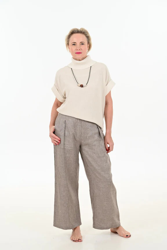  A woman wearing the Cleo Top by Julei Design in Natural, with light trousers, standing in front of a white background 