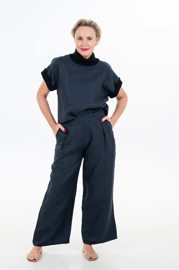 A woman wearing the Cleo Top by Julei Design in Navy with dark trousers, standing in front of a white background 