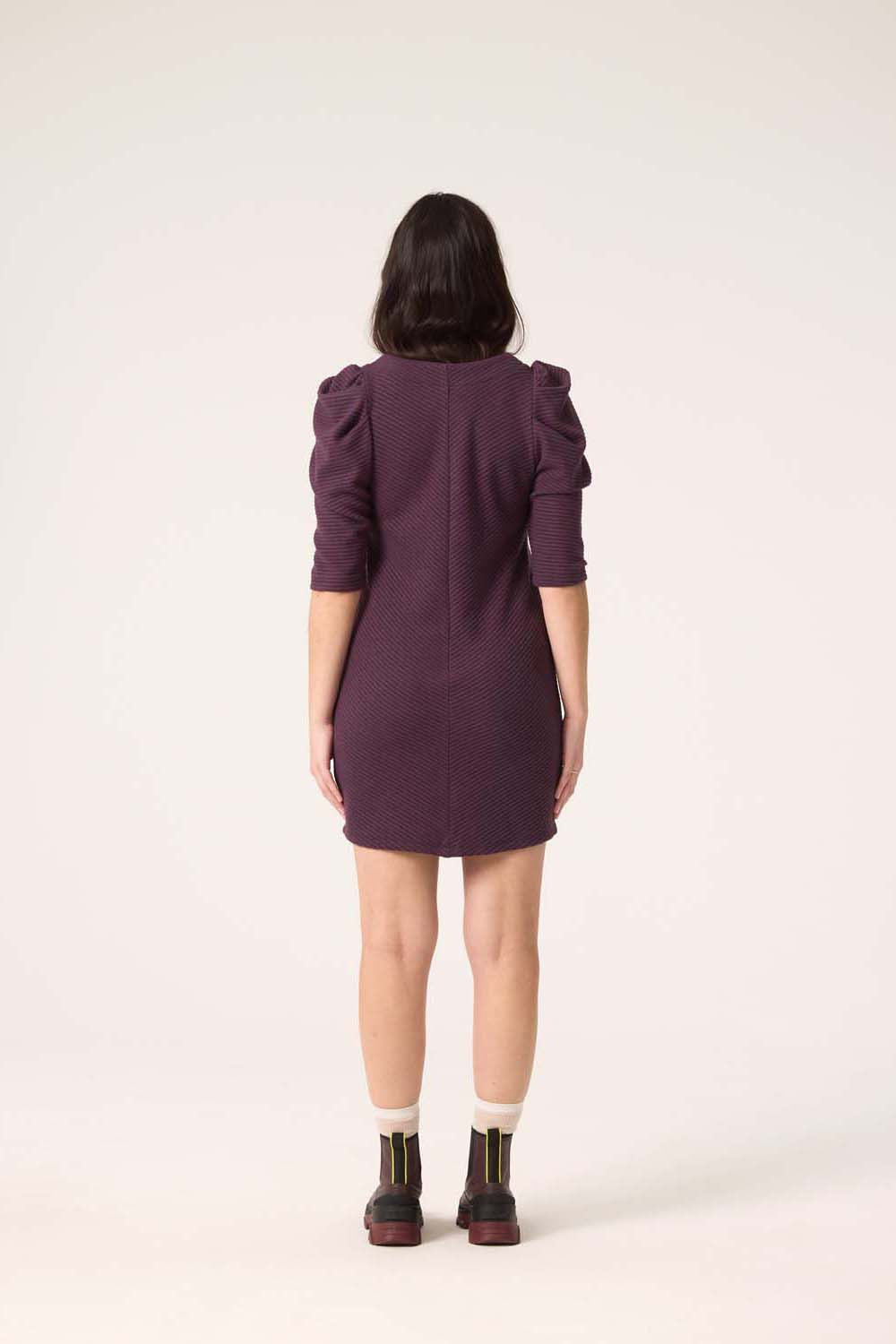 Back view of a woman wearing the Celeste Dress by Cokluch in Blackberry, standing in front of a white background