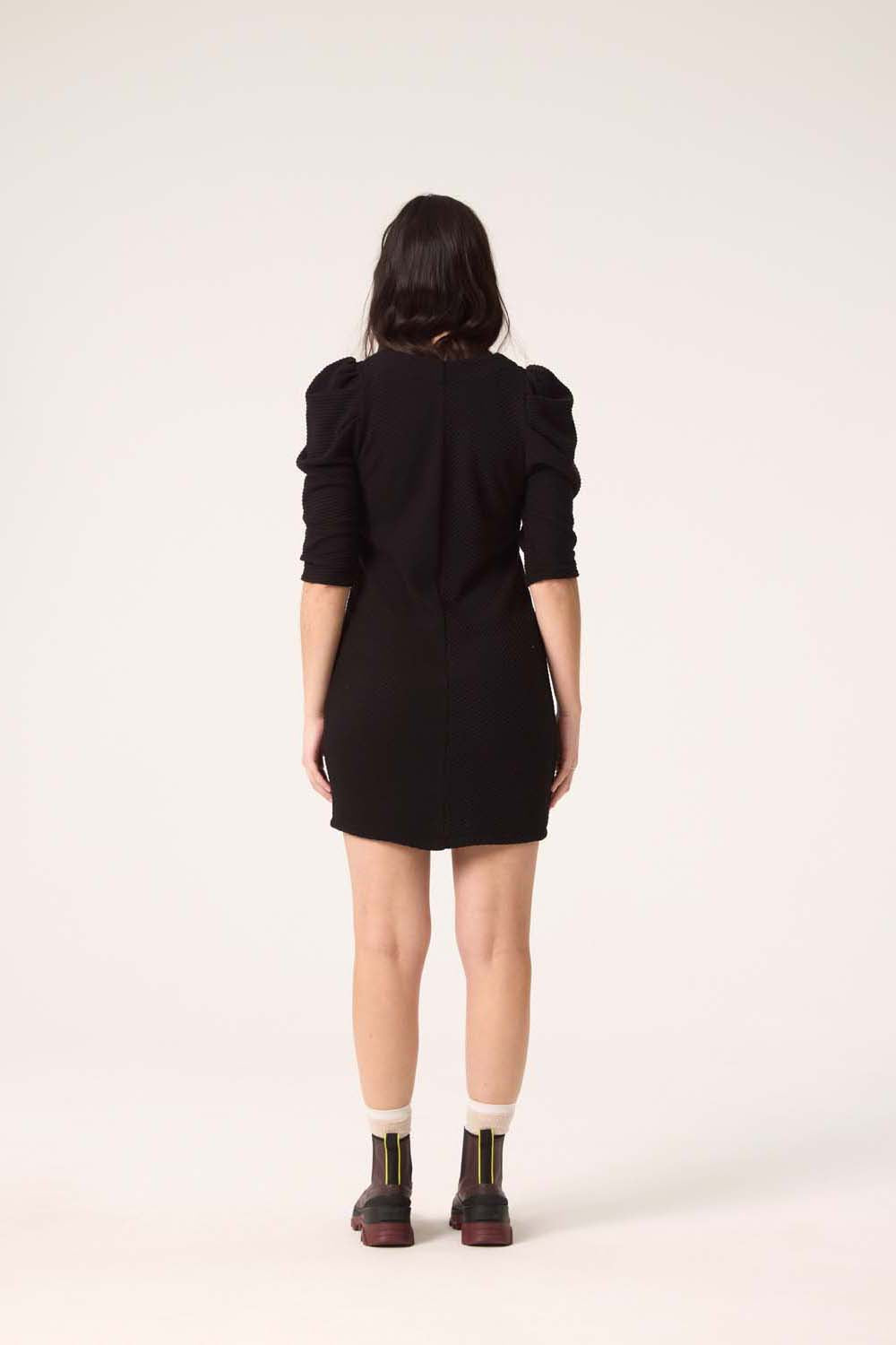 Back view of a woman wearing the Celeste Dress by Cokluch in Black, standing in front of a white background