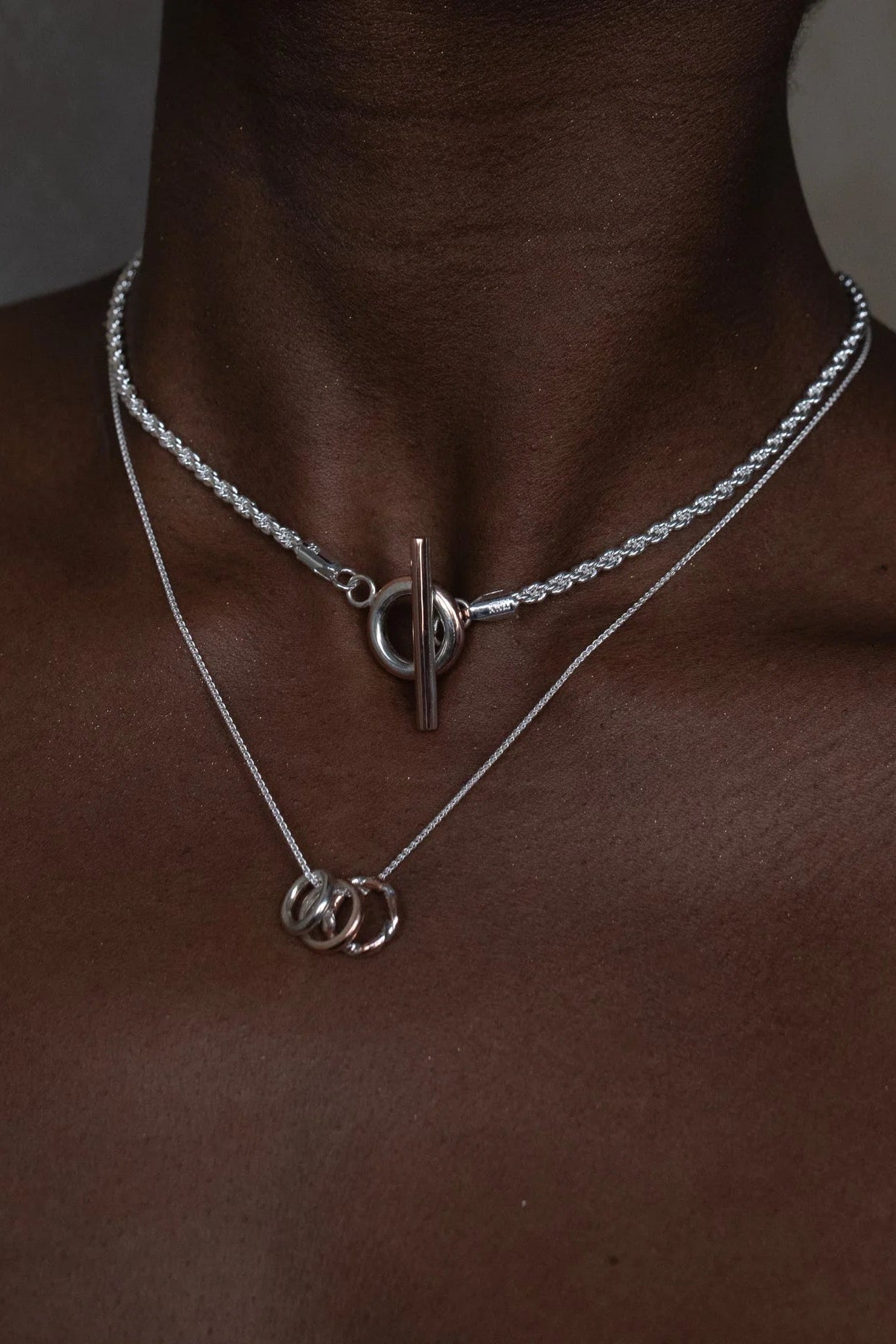 Close up of a woman wearing the Claudine Moncion Stack14 necklace in sterling silver and copper layered with a silver necklace. 