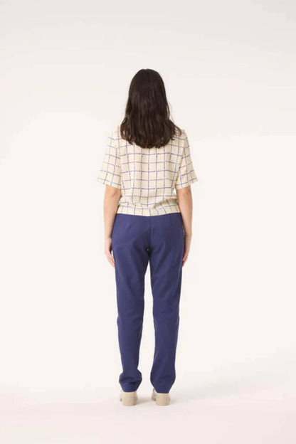 Back view of woman wearing the Sideral Top by Cokluch in Cream Plaid with blue pants, standing in front of a white background 