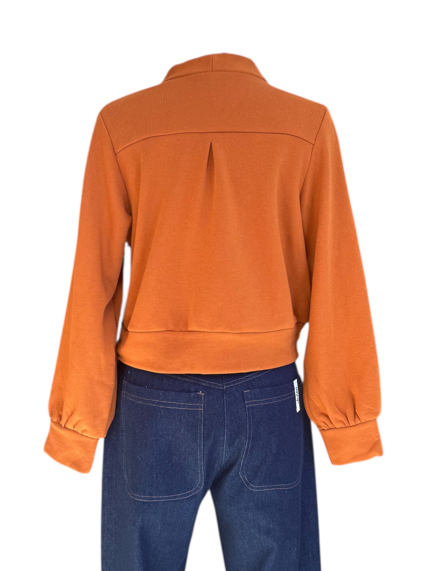 A back view of the Douglas Fleece Cardigan by Eve Lavoie in Pumpkin, a short cardigan with tortoiseshell buttons and a wide waistband, is shown with jeans on a mannequin against a white background