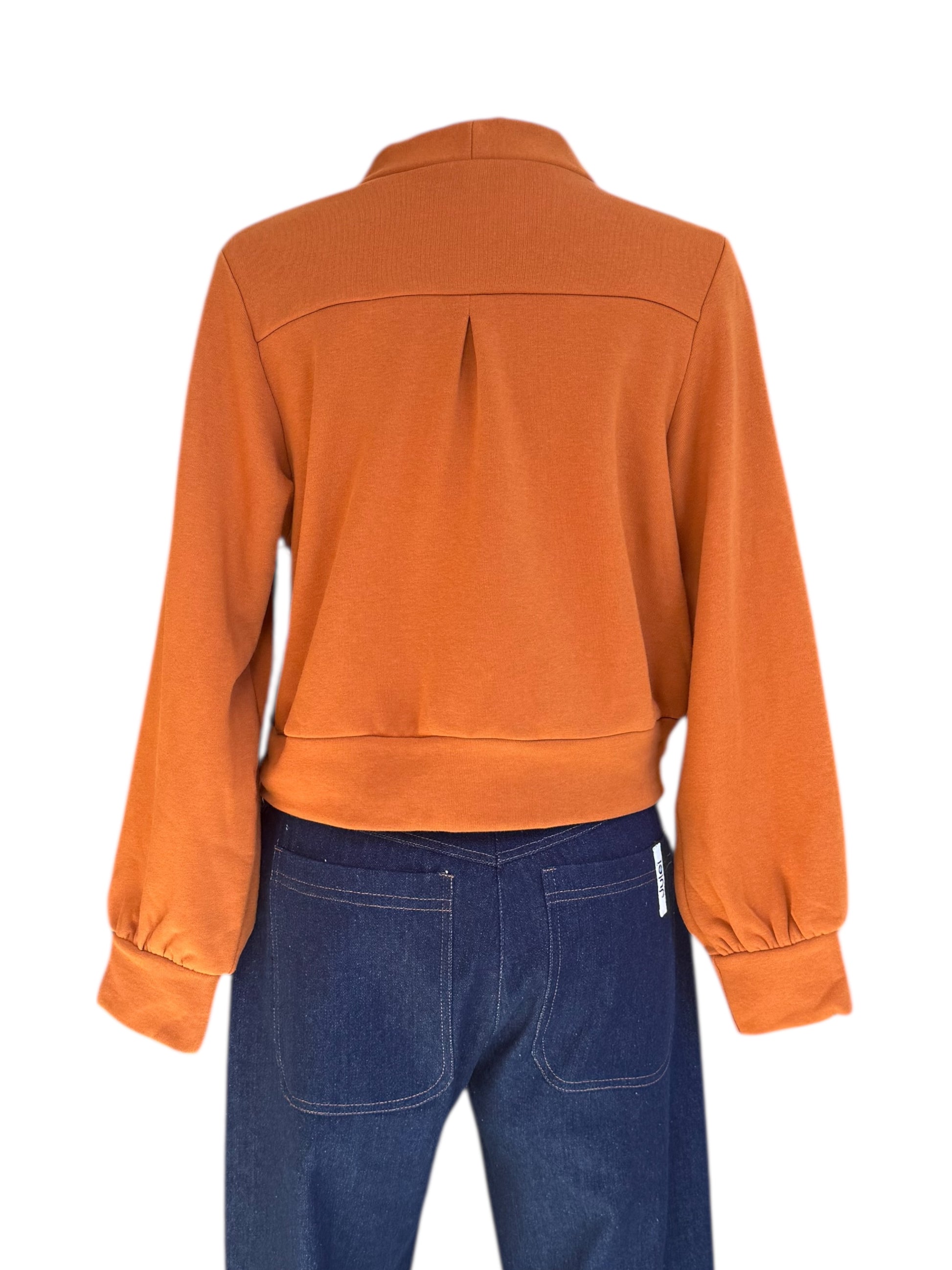 A back view of the Douglas Fleece Cardigan by Eve Lavoie in Pumpkin, a short cardigan with tortoiseshell buttons and a wide waistband, is shown with jeans on a mannequin against a white background