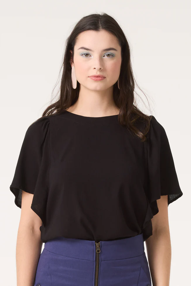 A woman wearing the Divine Top by Cokluch in Black, featuring a round neck and short ruffled sleeves, with a blue skirt. 