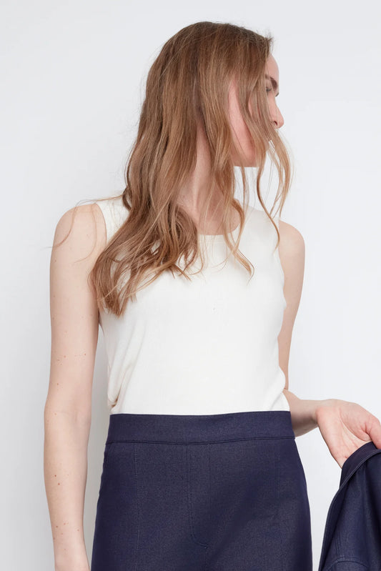 Close up of a woman wearing the Lucille Tank by Julei in Natural White, a ribbed tank with a round neck. She is wearing it with denim pants and holding a denim jacket in her hand. 