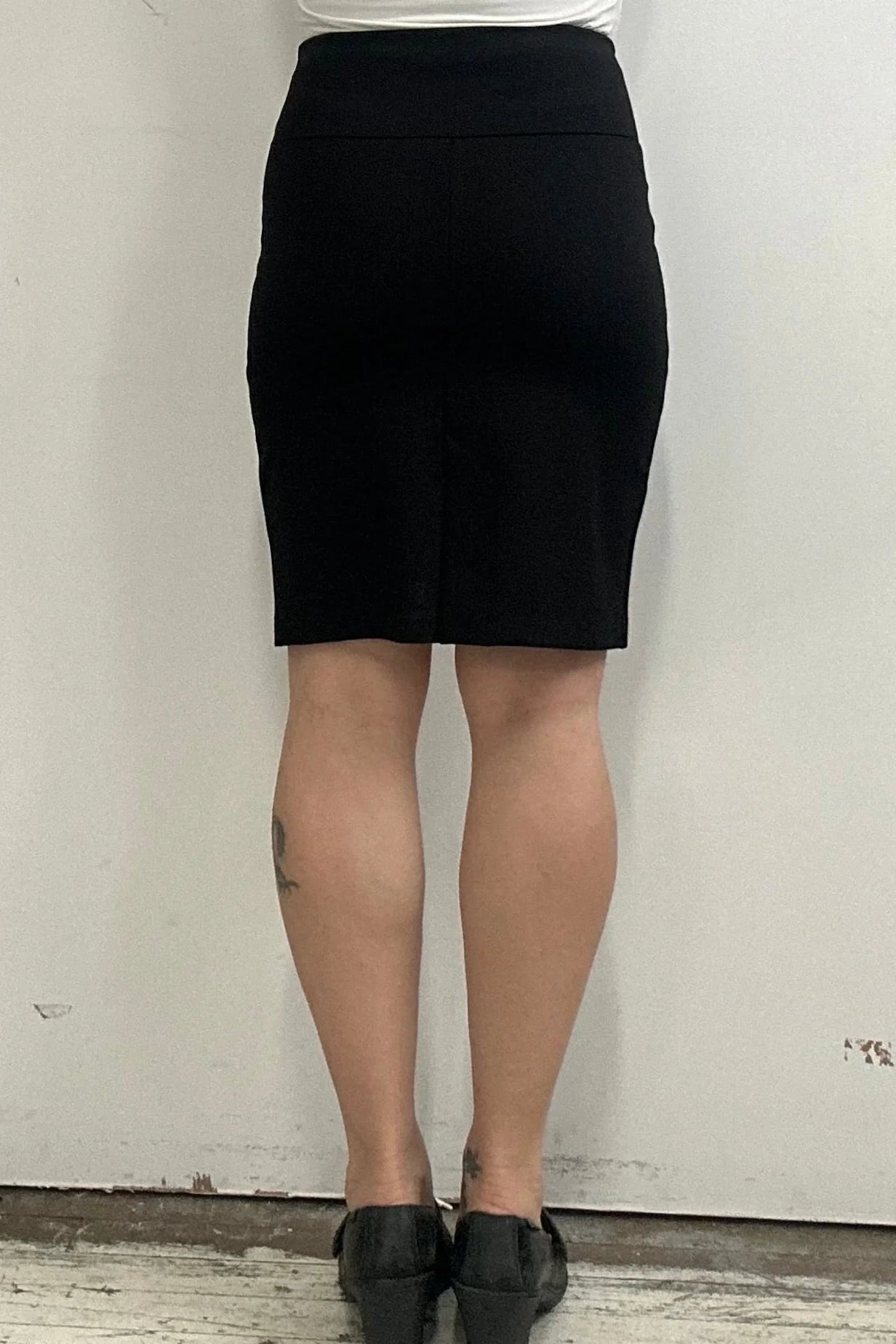 Waist down back view of a woman wearing the Veneto Skirt by Kollontai in Black, a pencil skirt with a wide-pull on waistband that hits above the knee.