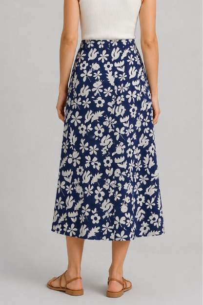 Back waist down view of a woman wearing the Chertsey Skirt by Message Factory in blue and white Summer Print, a midi-length A-line skirt with a wide pull-on waistband. She is wearing it with a white top and standing in front of a white background. 