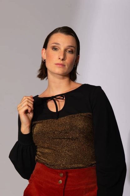 A woman wearing the Spike the Senses Reversible Top by Eve Lavoie in Gold Sparkle, with a cutout opening and tie detail and puffed sleeves