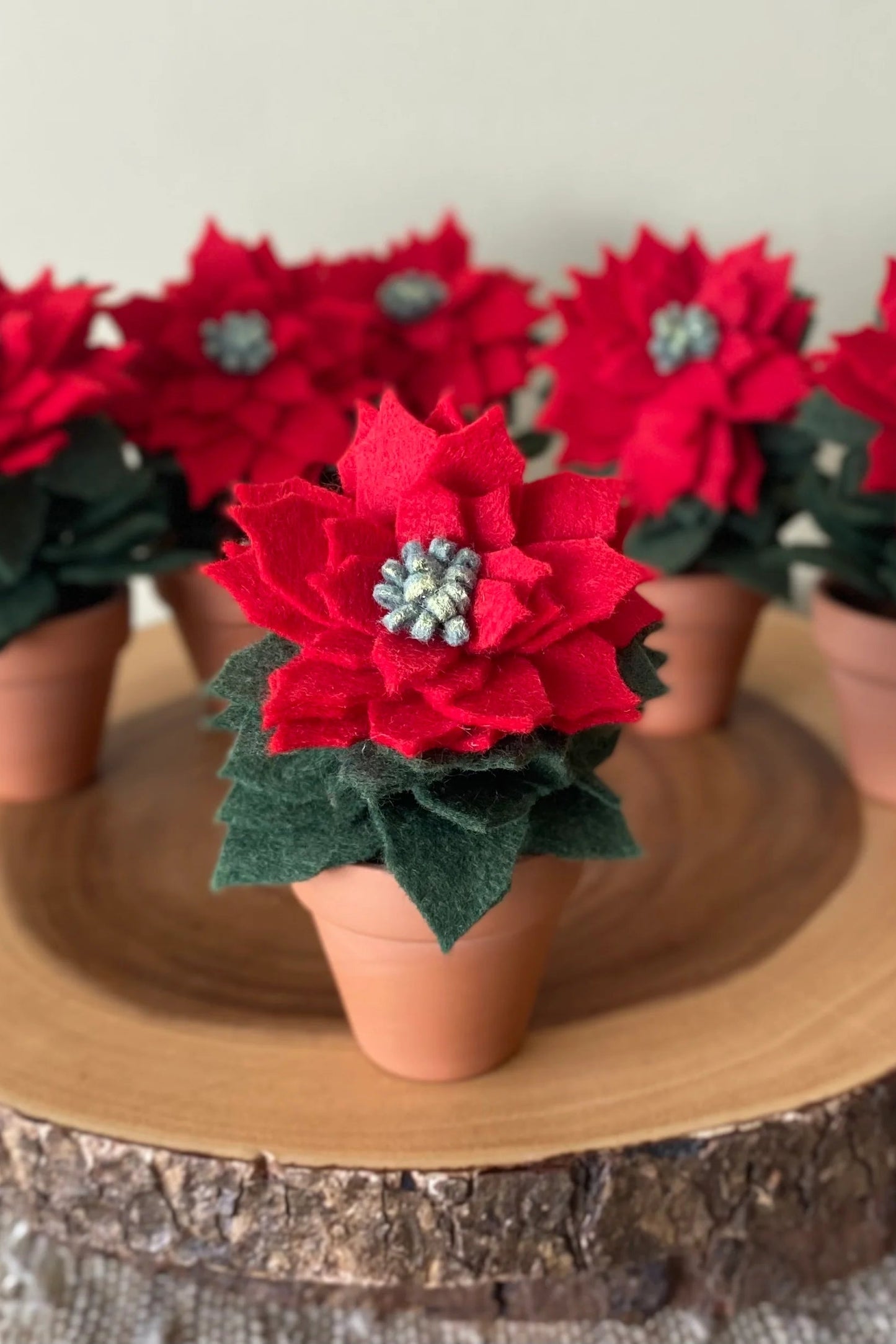 The Holiday Felt Poinsettia by ForgetBKnot is shown on a log against a white background. 