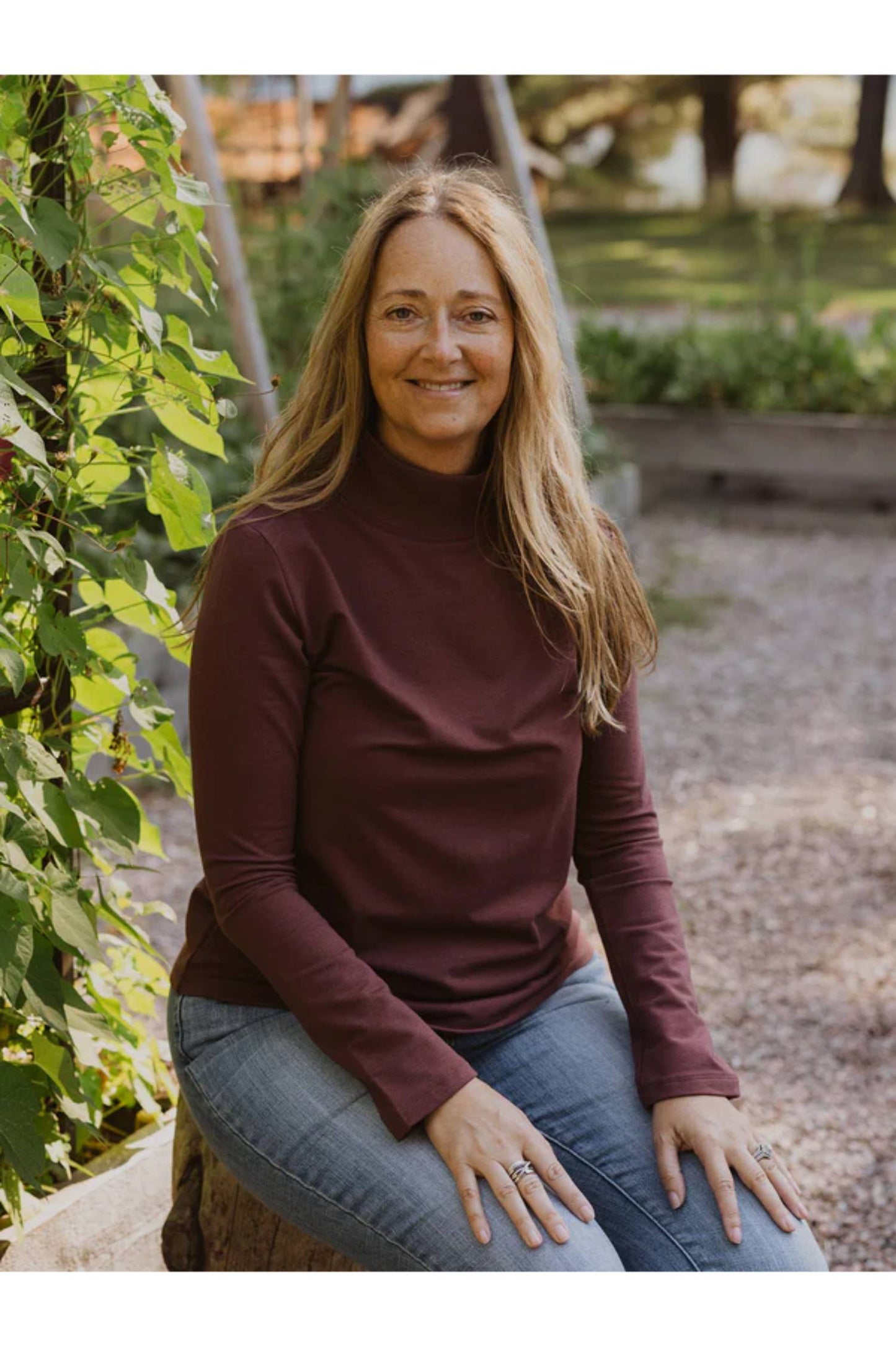 A close up of a woman wearing the Fauna Sweater by Blondie in Berry, featuring an A-line shape, belled sleeves, and a mock rib neck. 