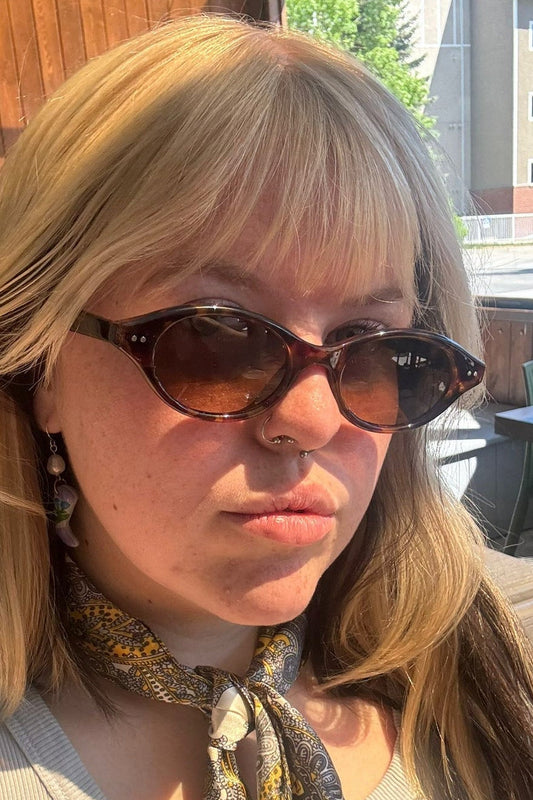 A woman wearing the Charly Sunglasses by Jenny Be Free, sitting on a patio