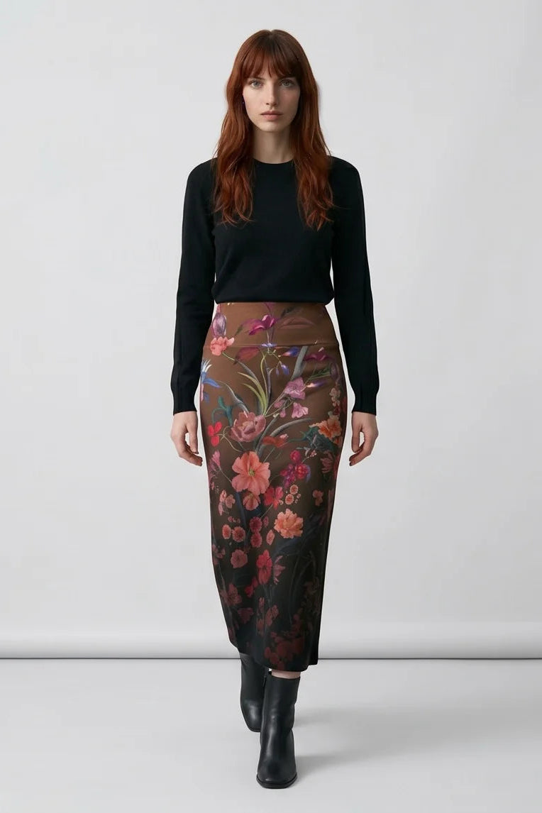 A woman wearing the Charlotte SKirt by Kollontai, a long slim cut brown skirt adorned with a floral pattern. She is wearing it with a black top against a white background