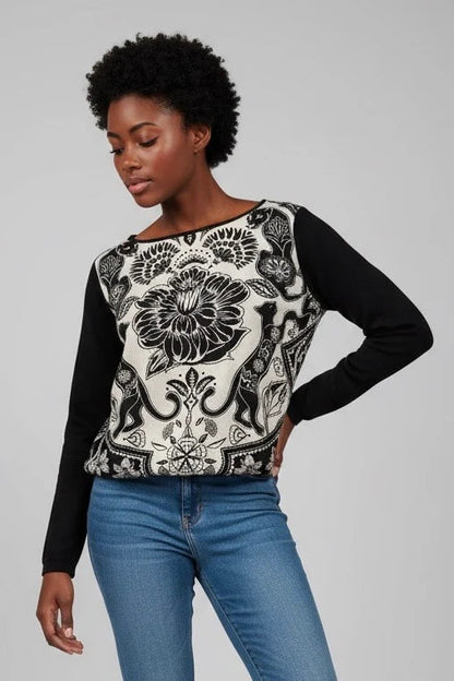 A woman wearing the Oriane Blouse by Kollontai, featuring a black-on-ivory floral and panther print, solid black long sleeves and back, and an elasticized hem. She is wearing it with jeans and standing in front of a white background. 