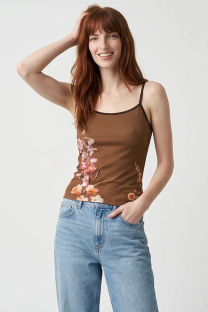 A woman wearing the Morganne Top by Kollontai, a brown floral tank top with spaghetti straps. She is wearing it with blue jeans against a white background