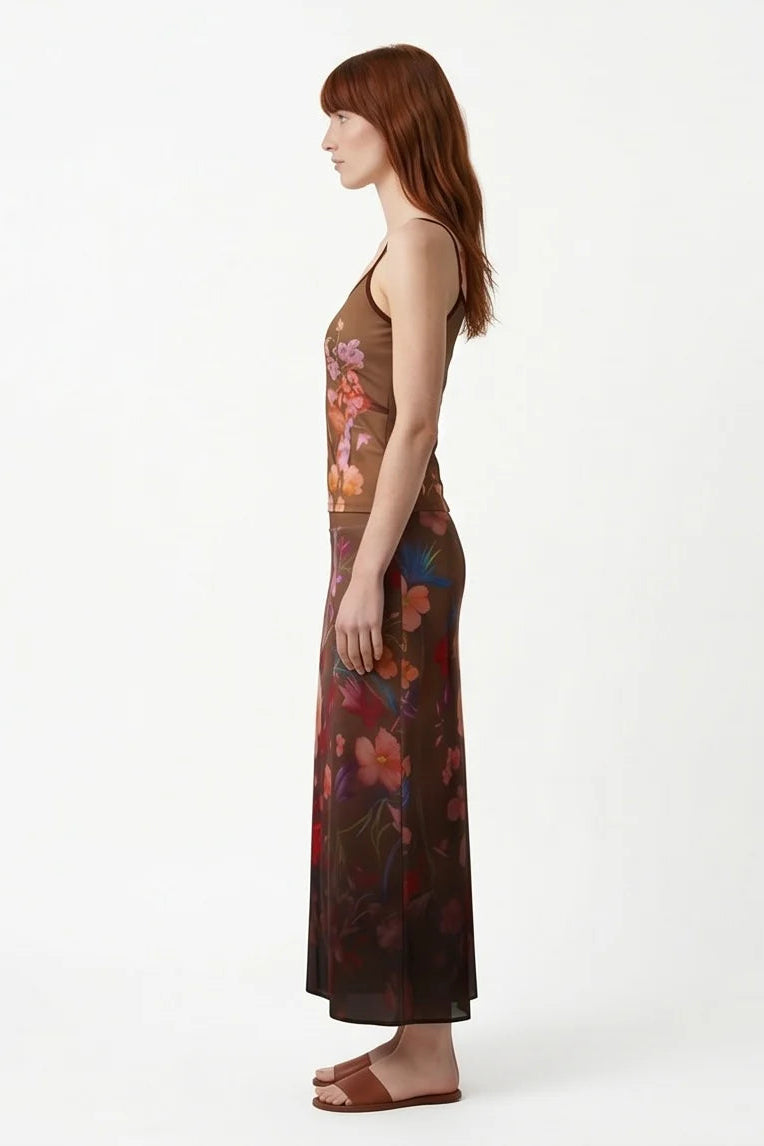 Side view of a woman wearing the Charlotte SKirt by Kollontai, a long slim cut brown skirt adorned with a floral pattern. She is wearing it with the matching Morganne Top against a white background