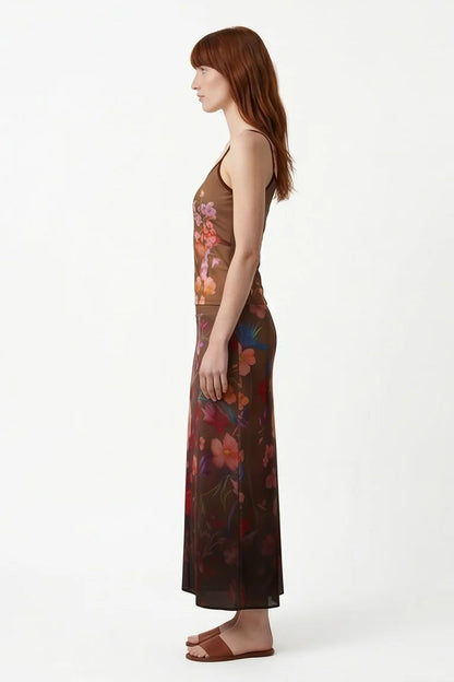 Side view of a woman wearing the Charlotte SKirt by Kollontai, a long slim cut brown skirt adorned with a floral pattern. She is wearing it with the matching Morganne Top against a white background