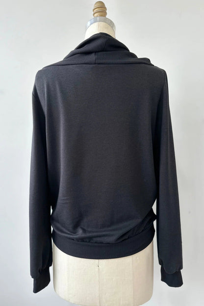 A back view of the Jullian Sweater by Kollontai in Black, with a cowl neck, long sleeves, and a kangaroo pocket, is shown on a mannequin in front of a white background. 