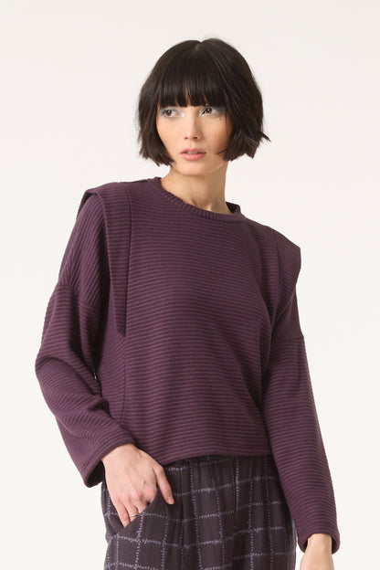 Semi close-up of a woman wearing the Galactic Sweater by Cokluch in Blackberry, standing in front of a white background