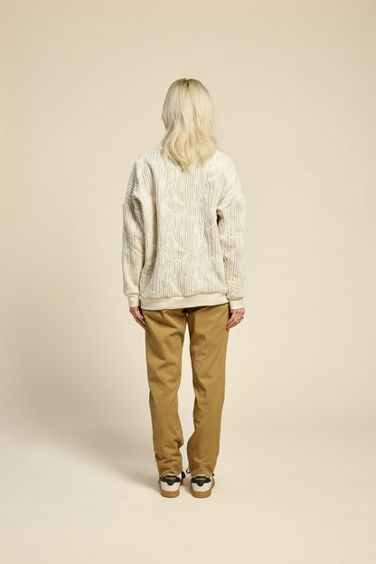 Back view of a woman wearing the Hotel Sweater by Cokluch in Natural, a loose fitting round necked sweater in Crinkle Max fabric. She is wearing it with yellow pants and standing in front of a beige background. 