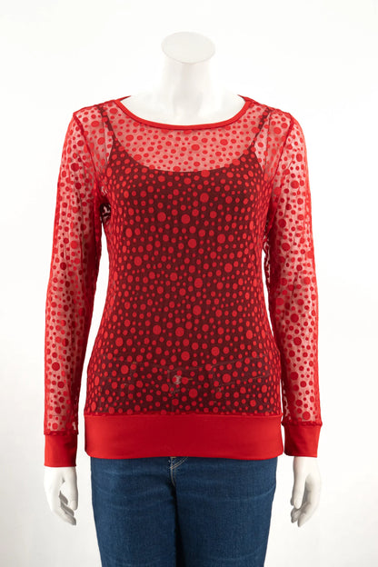 The Daisy Lace Top by Karkass in Grenade in shown on a mannequin with jeans against a white background. It's a long sleeved shirt with a round neck in sheer red mesh with a polka dot pattern.
