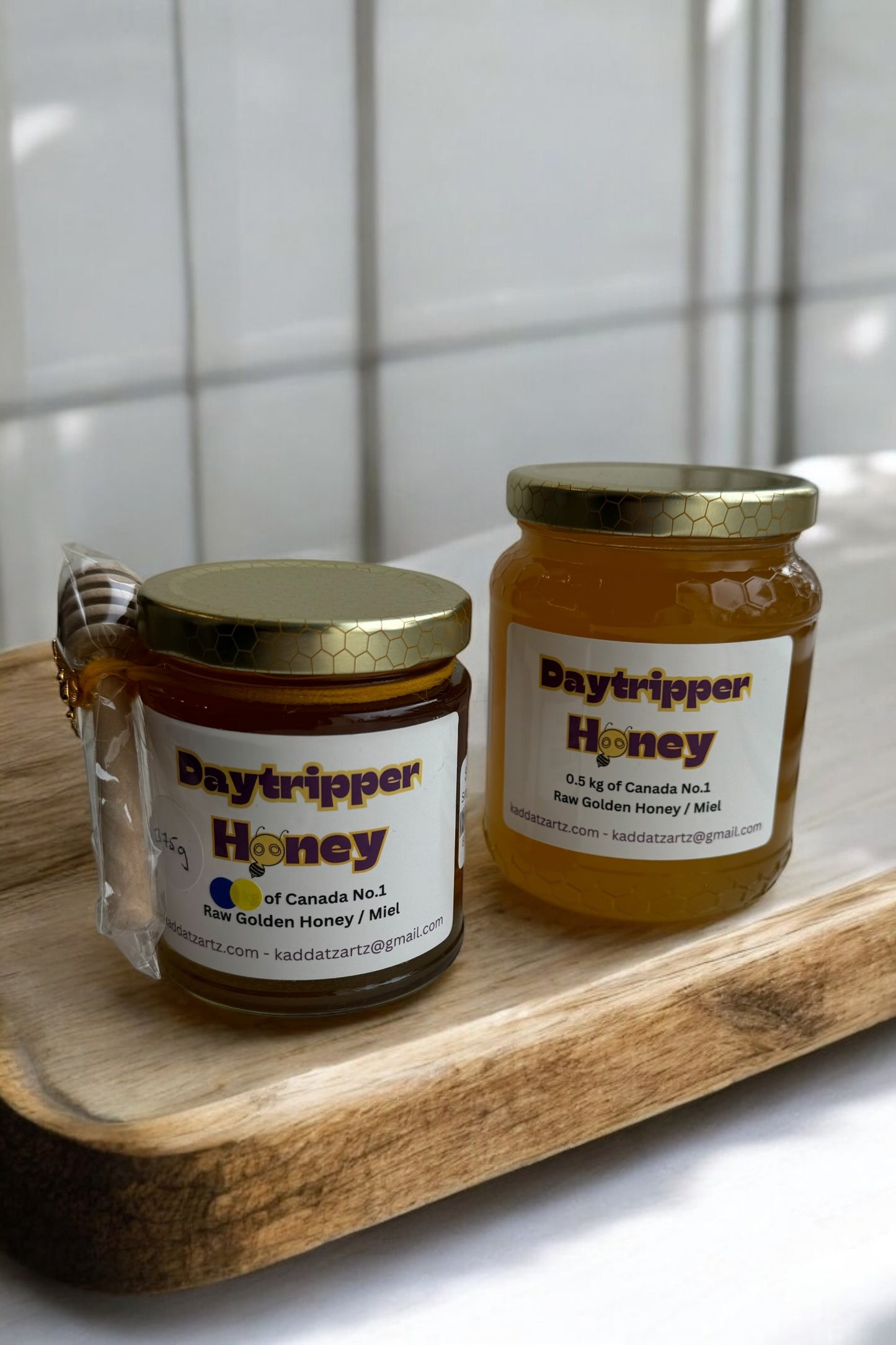 Jars of Daytripper Honey by Kaddatz are shown on a wooden cutting board in front of a tiled wall. 