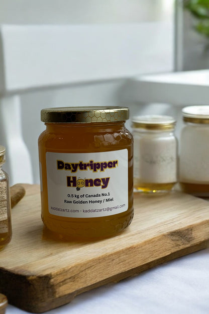 A jar of Daytripper Honey by Kaddatz is shown on a wooden cutting board in front of a tiled wall. 