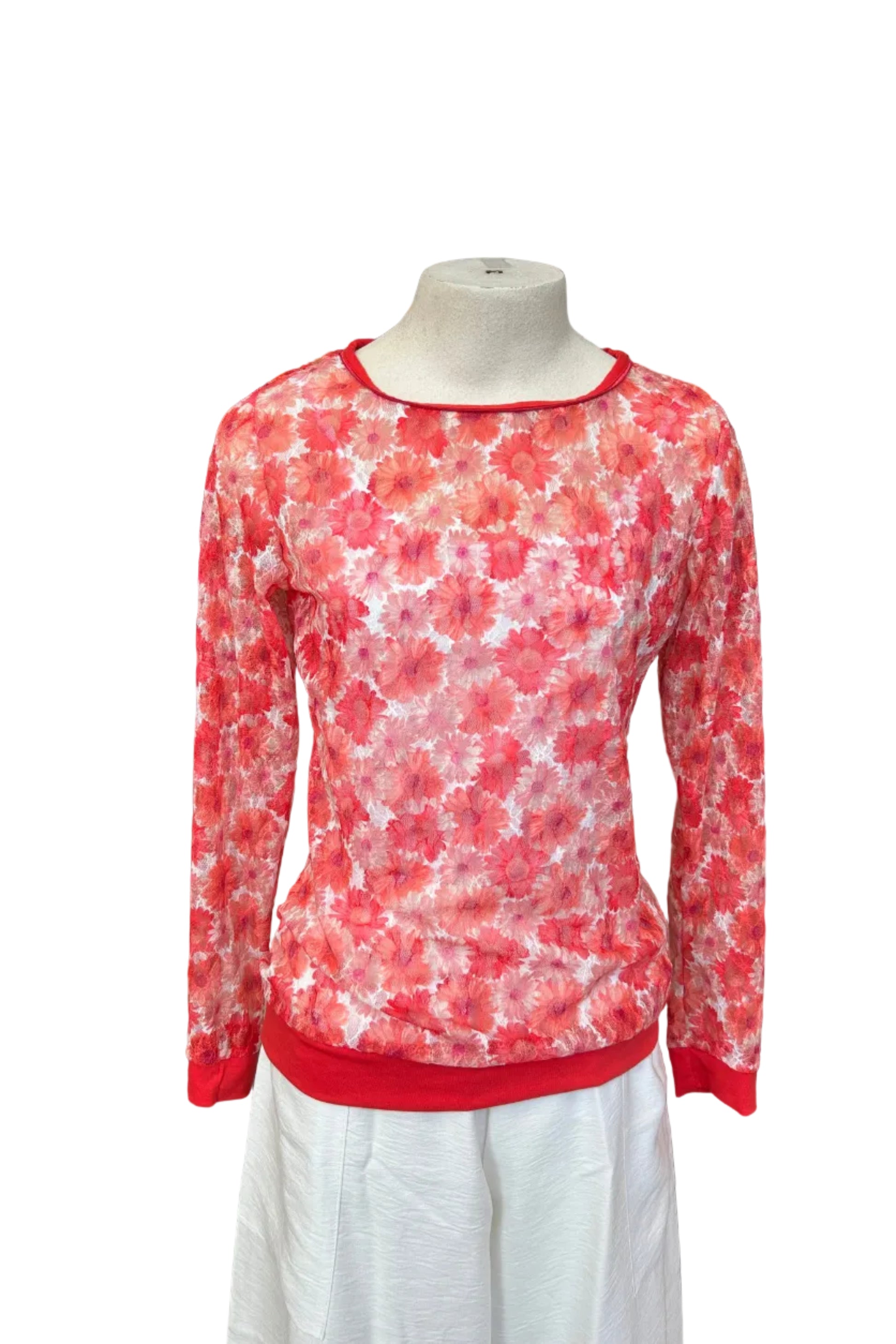 The Daisy Lace Shirt by Karkass in Coral, a floral lace shirt with solid cuffs and hem, is shown over a white tank and with white pants against a white background. 