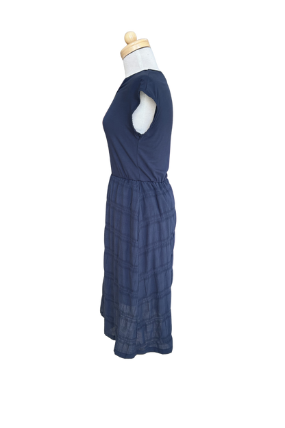 A side view of the Mona Dress by Tangente in Navy, a below the knee length dress featuring a bamboo rayon bodice and seersucker skirt, with short sleeves and a round neck, is shown on a mannequin against a white background. 