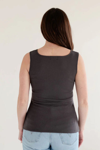 Back view of a woman wearing the Ang Hill Tracey Tank in Charcoal with wide straps, ribbed fabric, and a square neckline. She is wearing it with jeans and standing in a white room. 