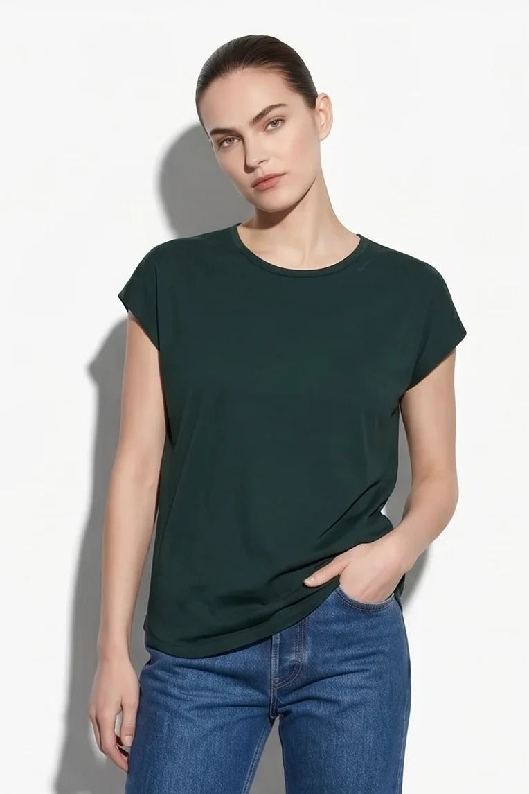 A woman wearing the Eowyn T-Shirt by Kollontai in Green with jeans standing against a grey background. 