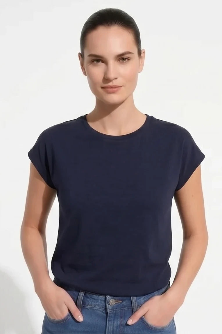 A woman wearing the Eowyn T-Shirt by Kollontai in Navy with jeans standing against a grey background. 