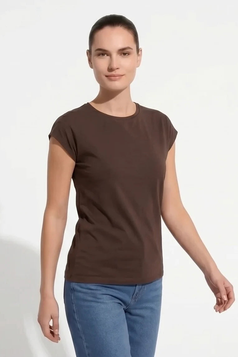 A woman wearing the Eowyn T-Shirt by Kollontai in Chocolate with jeans standing against a grey background. 