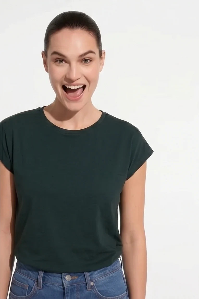 A woman wearing the Eowyn T-Shirt by Kollontai in Green with jeans standing against a grey background. 