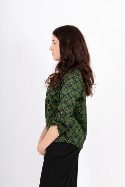 Side view of a woman wearing the Leonie Blouse by Infime in Black with Green print, featuring a notched V-neckline, three button placket, and 3/4 sleeves. She is wearing it with black pants and standing in front of a white background. 